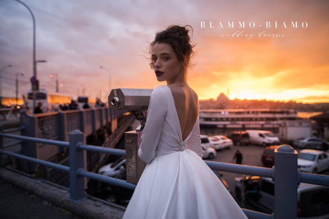 A bride wearing satin princess wedding dress Tilda by blammo-biamo with long sleeves, long train and open back with brooch by Rara Avis at Dell' Amore Bridal, Auckland, NZ. 1