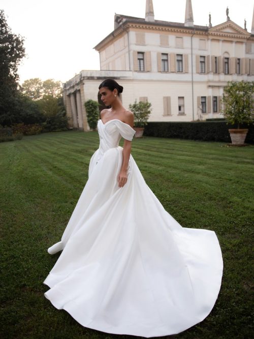Off-shoulder satin wedding dress Shedar with wrap-over drapery corset by rara avis at Dell'Amore Bridal, NZ. 1